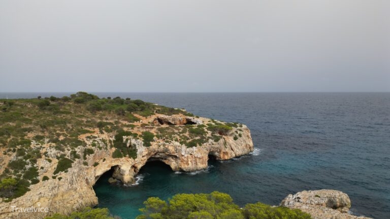Luftaufnahme der felsigen Küste bei Cala Varques mit Meereshöhlen und der Pont Natural im Hintergrund