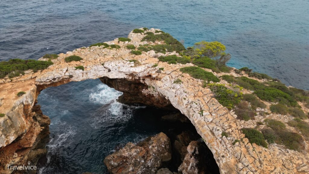 Luftaufnahme der natürlichen Felsbrücke bei Cala Varques mit Wellen unter dem Felsbogen