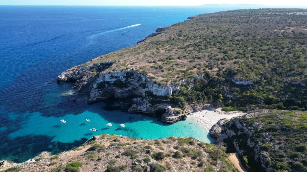 Weite Luftaufnahme der Cala Màrmols mit hellem Strand, türkisblauem Wasser und der unbebauten Felsküste