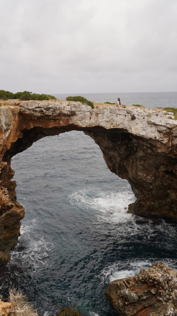 Hochformatblick auf die natürliche Felsbrücke und die Felsküste bei Cala Varques
